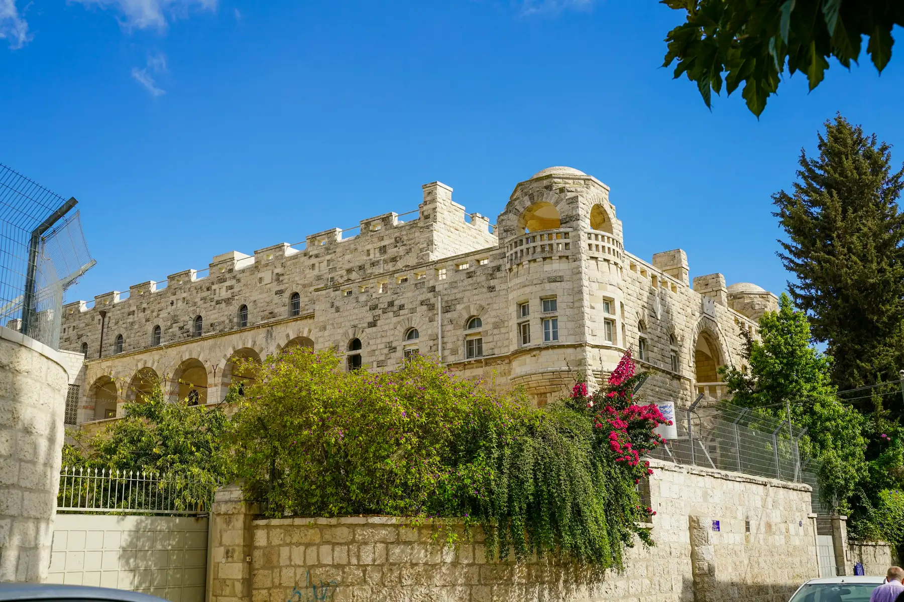 בניין אבן ירושלמי עם חלונות מקושתים, בין עצים ירוקים